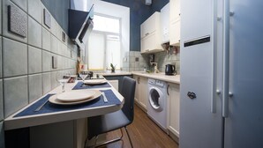 Una cocina compacta con lavadora integrada, un comedor con mesa y sillas, y un ventanal que aporta luz natural.