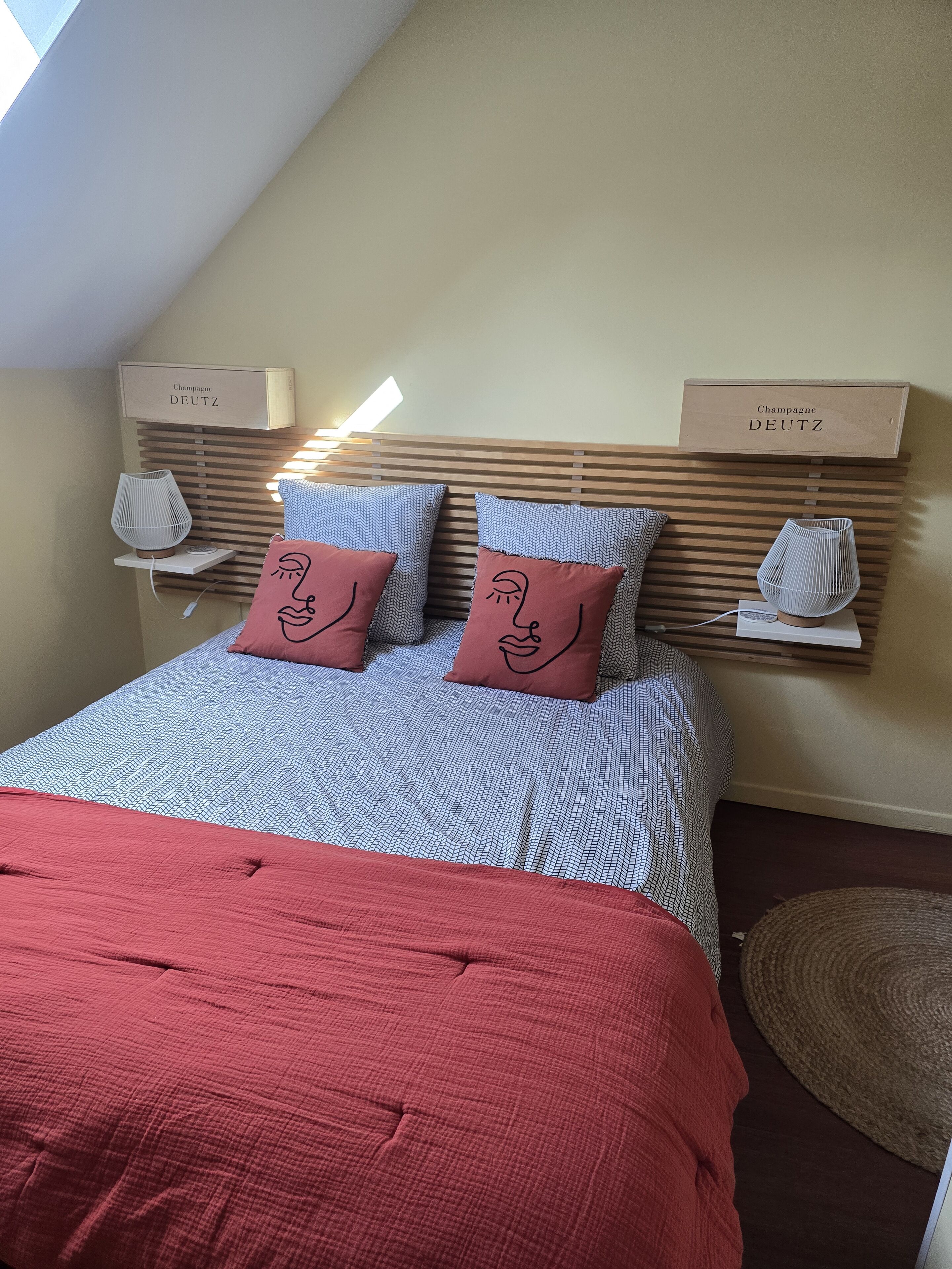 A neatly made bed with patterned bedding, two decorative pillows, a red throw blanket, and a bedside lamp.