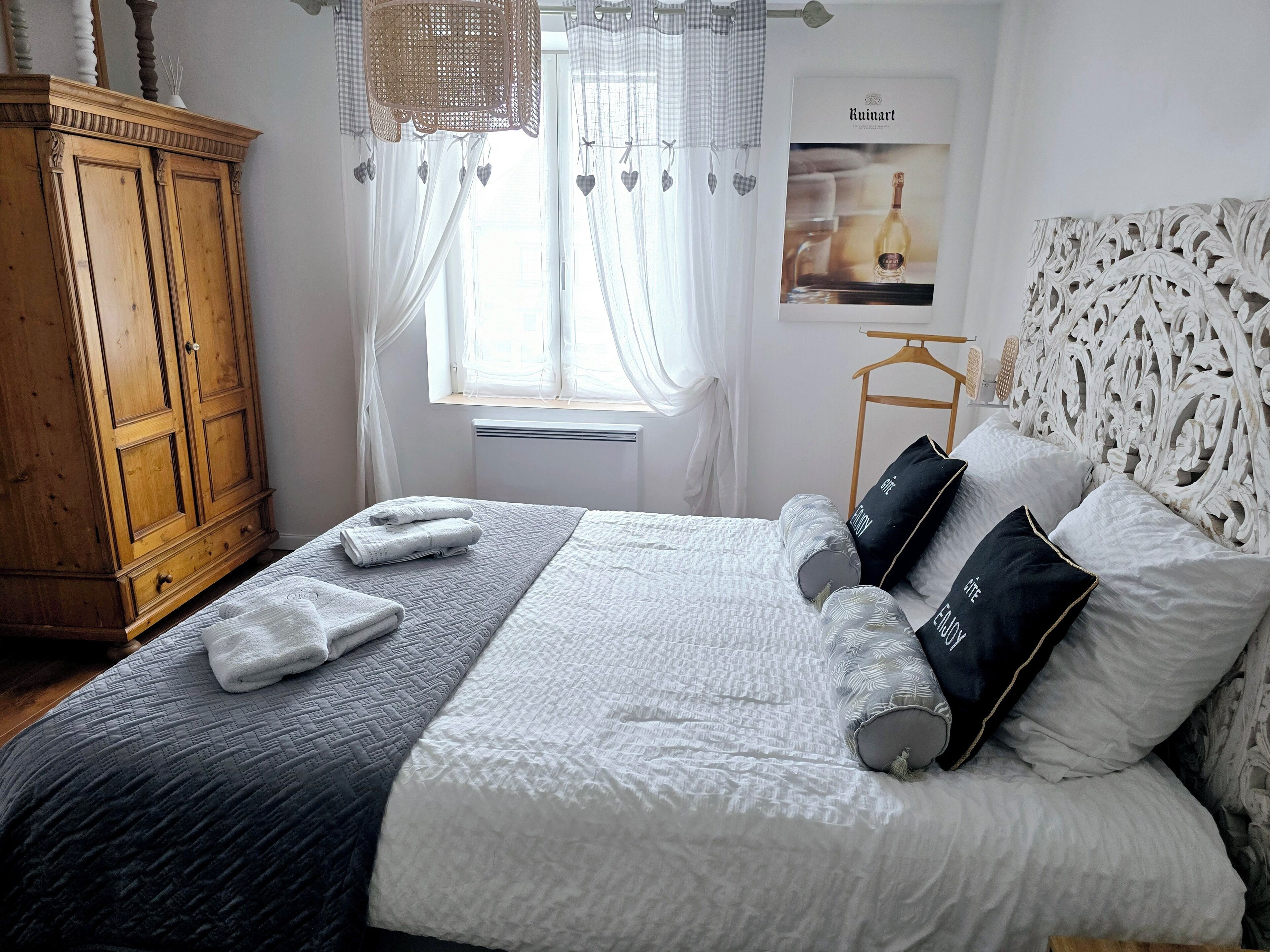 Un dormitorio ordenado con una cama grande, un armario de madera y una ventana con cortinas traslúcidas.