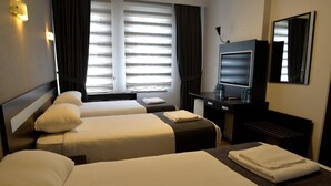Une chambre d’hôtel avec deux lits, un bureau avec une télévision et une fenêtre avec des stores.