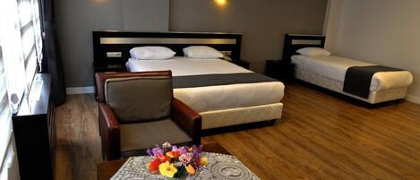 A hotel room with two beds, a desk, a chair, and a table with a vase of flowers.