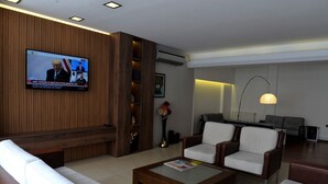 Un hall d’hôtel moderne doté d’un téléviseur diffusant les actualités, de sièges confortables et d’un piano.
