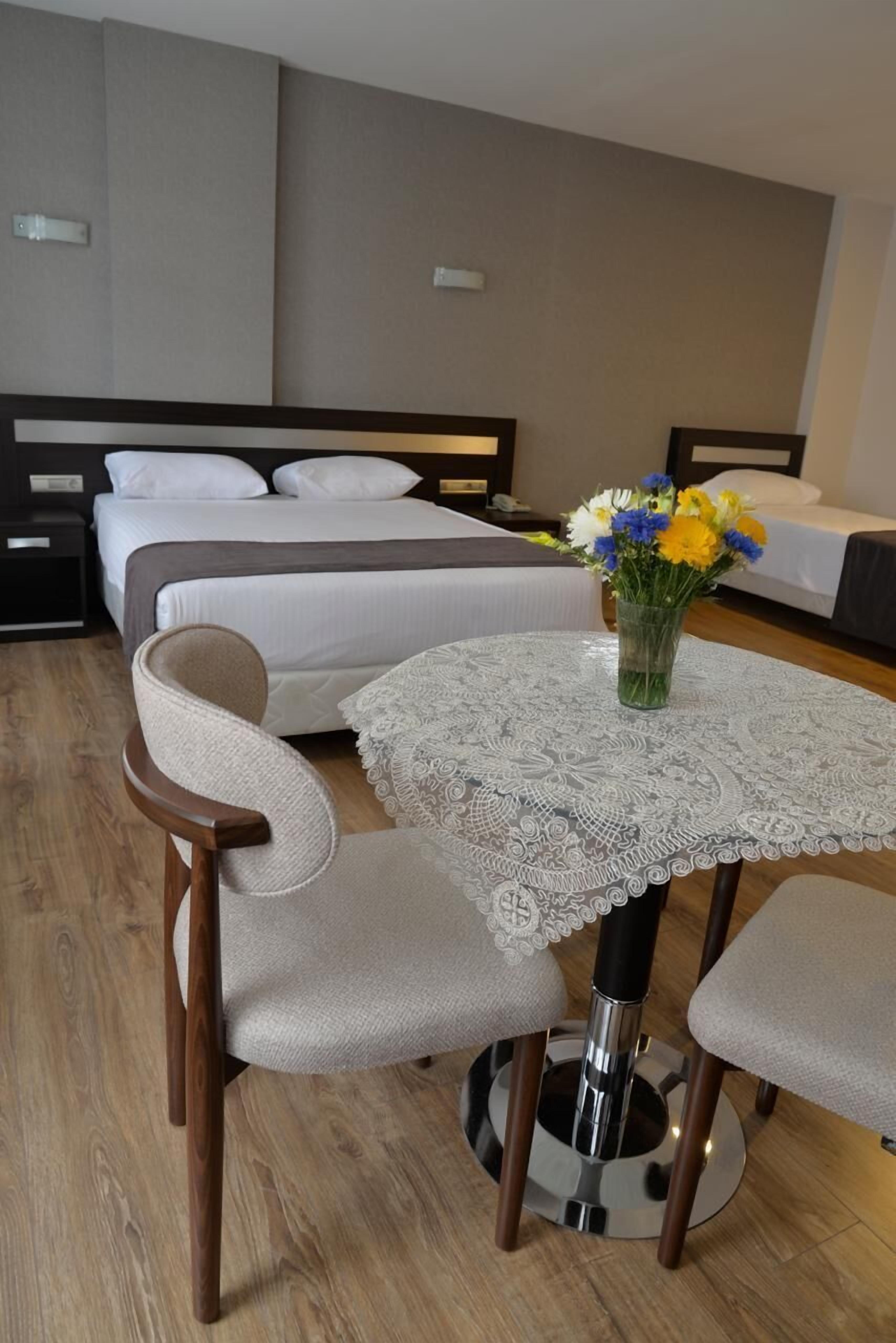 A hotel room with a bed, a round table with chairs, a vase with flowers, and a nightstand.