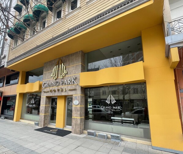 The exterior of the Grand Park Hotel with a yellow facade and large windows.