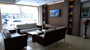 Un hall d’hôtel moderne avec un canapé, des fauteuils, une table basse et un téléviseur fixé au mur.