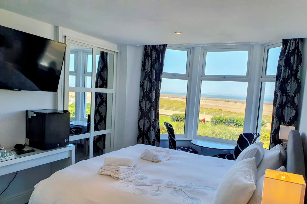 A hotel room with a bed, a TV, a desk with a computer, and a view of the beach.