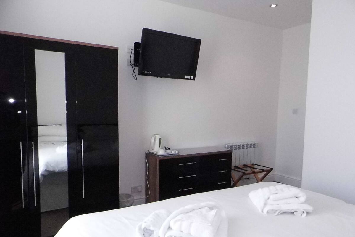A hotel room with a bed, a TV mounted on the wall, a dresser, and a radiator.