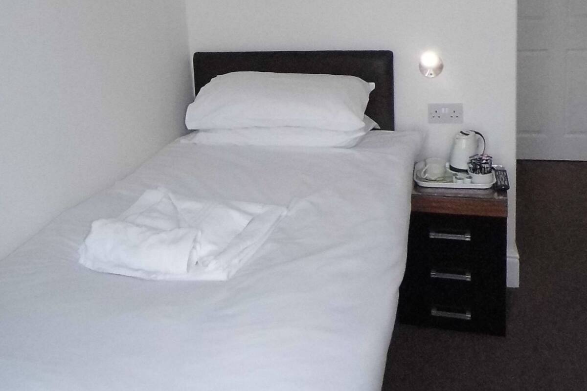 A neatly made bed with white linens, a bedside table with a lamp, and a power outlet on the wall.