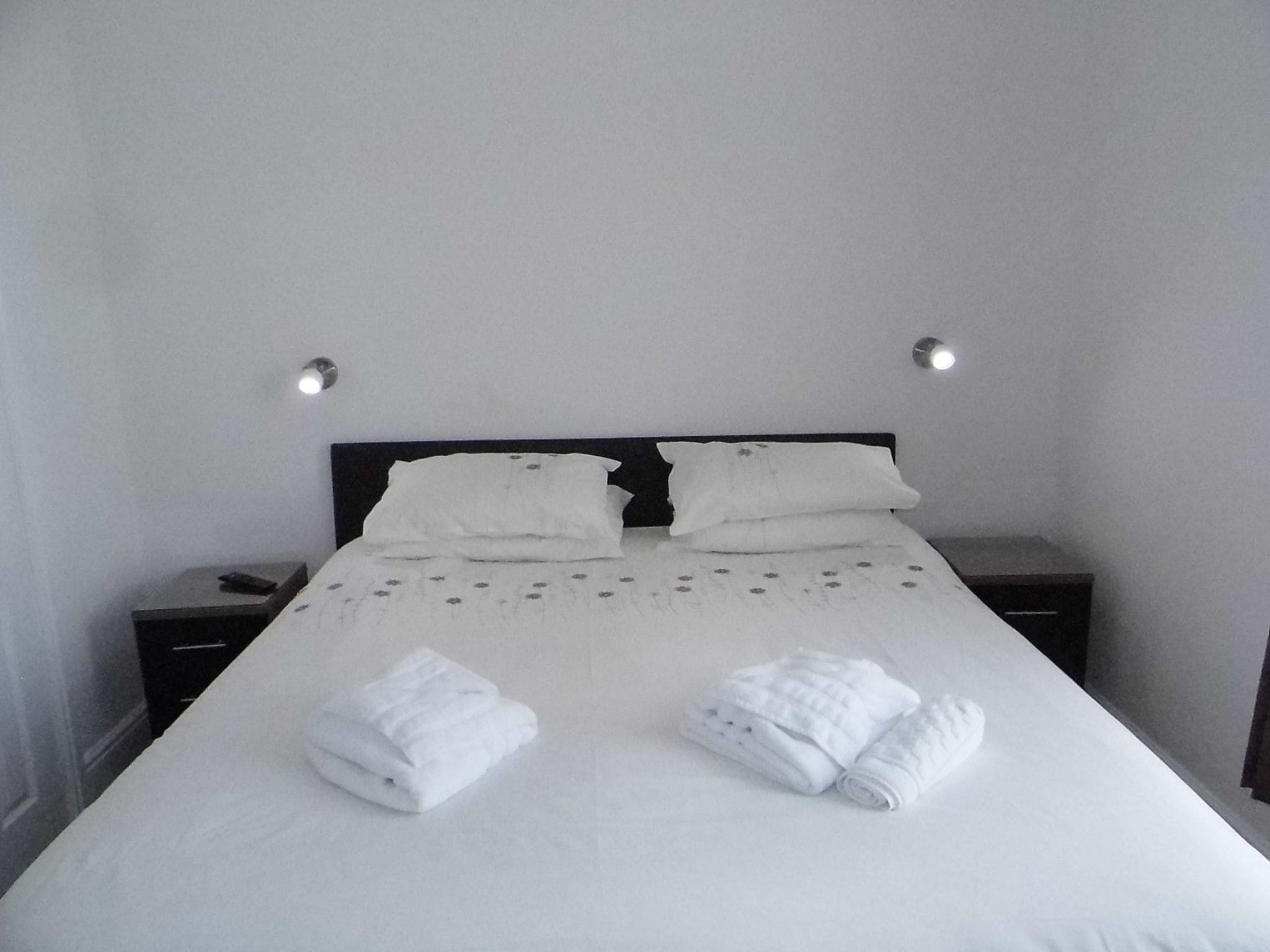 A neatly made bed with white linens and two pillows, two bedside tables with lamps, and a folded towel on the bed.