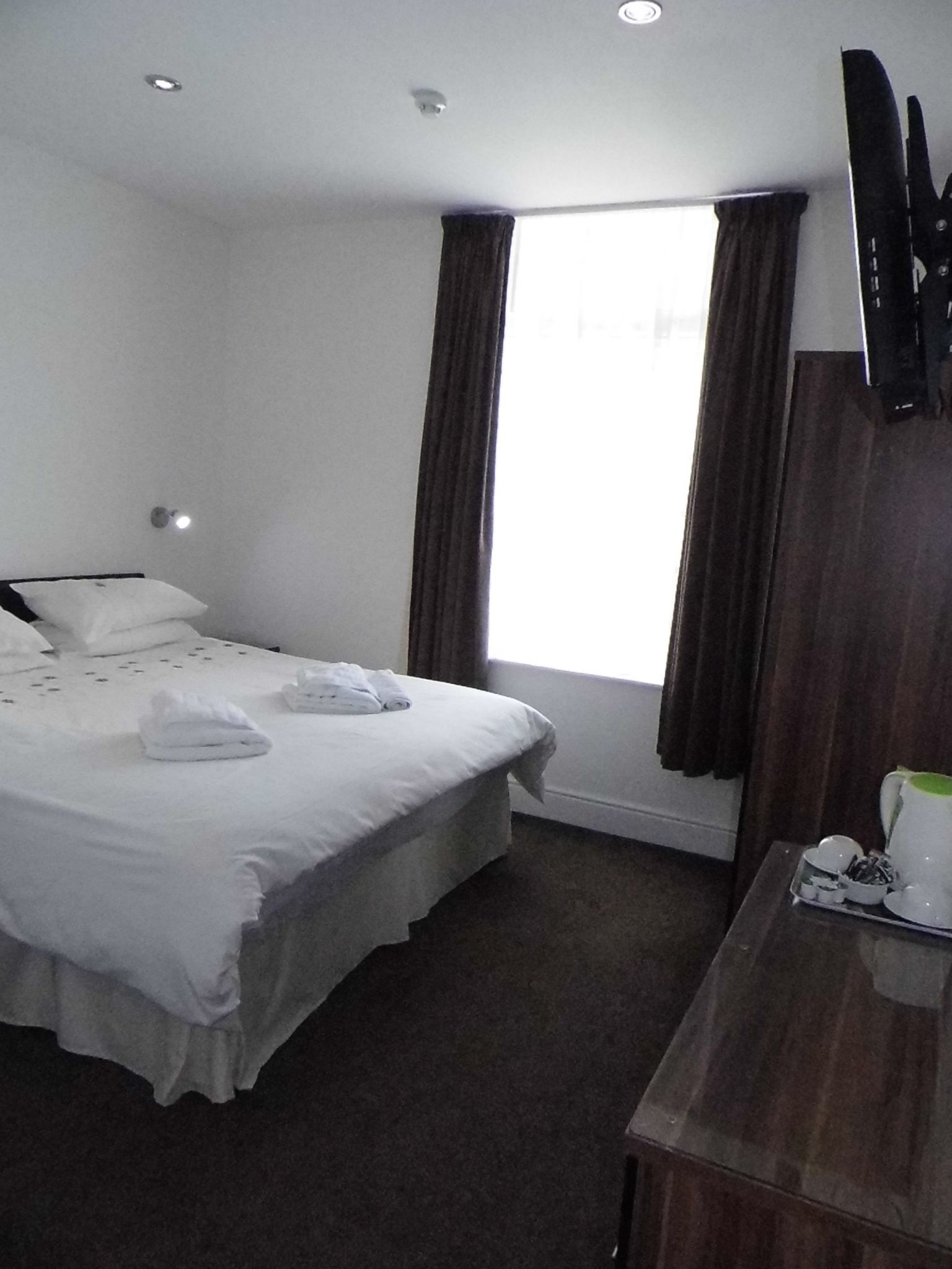 A hotel room with a bed, a desk, a mirror, and a window with curtains.