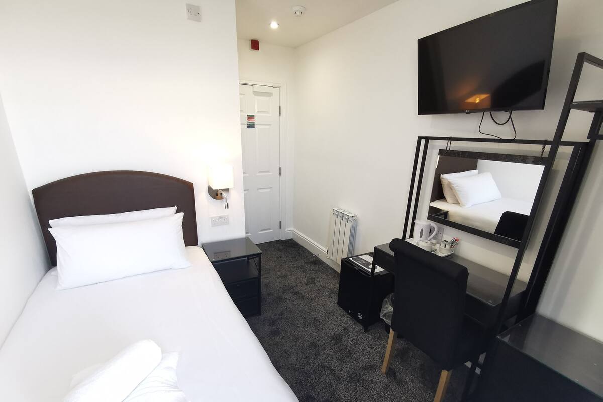 A hotel room with a bed, a desk with a chair, a TV, and a mirror.