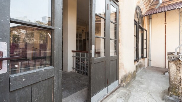 A narrow courtyard with a wooden door and windows, a metal railing, and a tiled roof.
