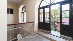 A corridor with a metal railing, a large black door with glass panels, and a view of a red-roofed building outside.