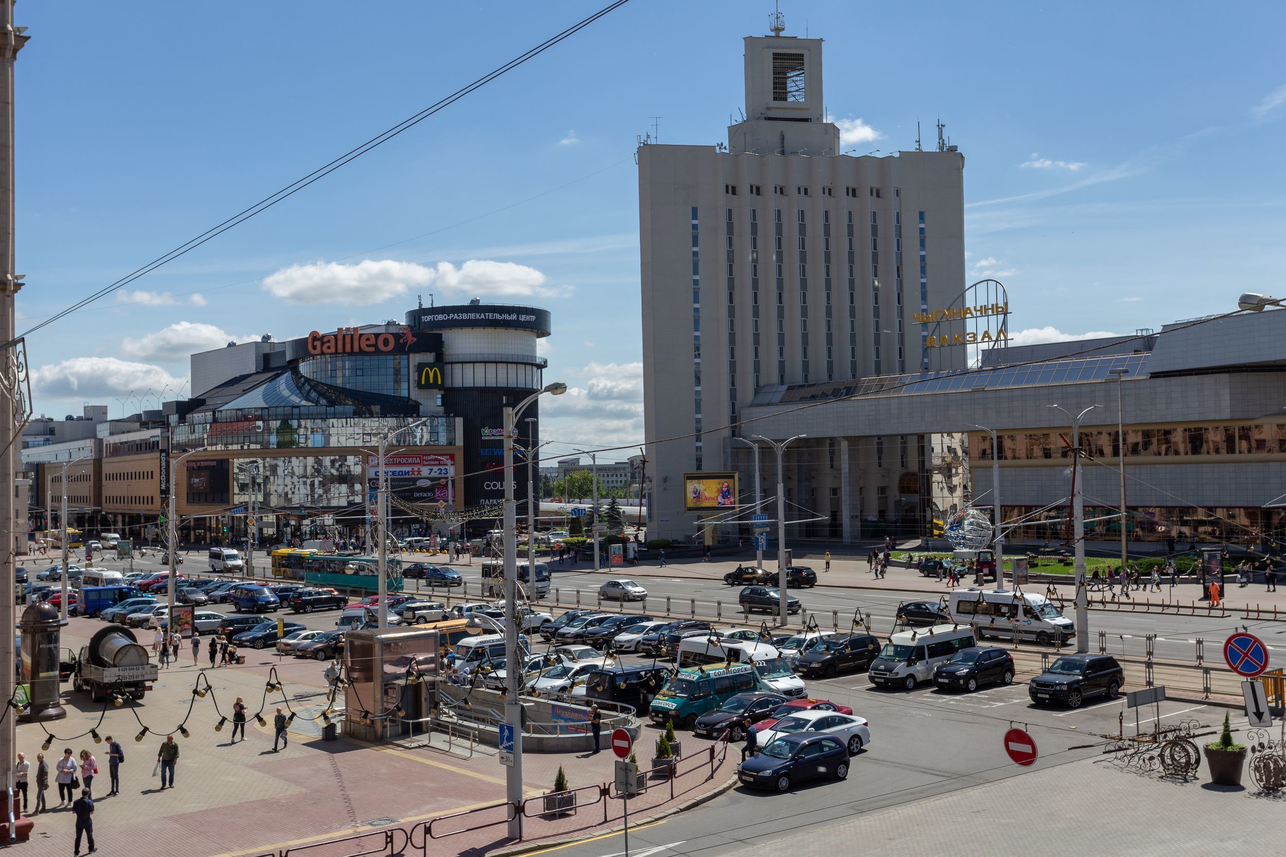 A busy urban intersection with a large building featuring a prominent sign for 'Galileo' and a McDonald's logo.