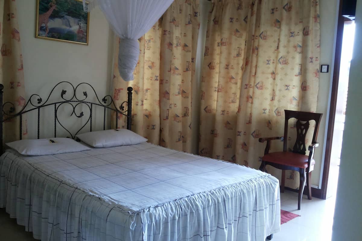 Un dormitorio con cama, cortinas, una silla y un cuadro en la pared.