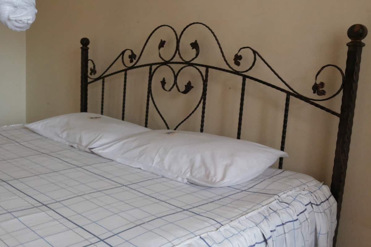 Una cama con cabecera de metal, almohada blanca y colcha a cuadros.