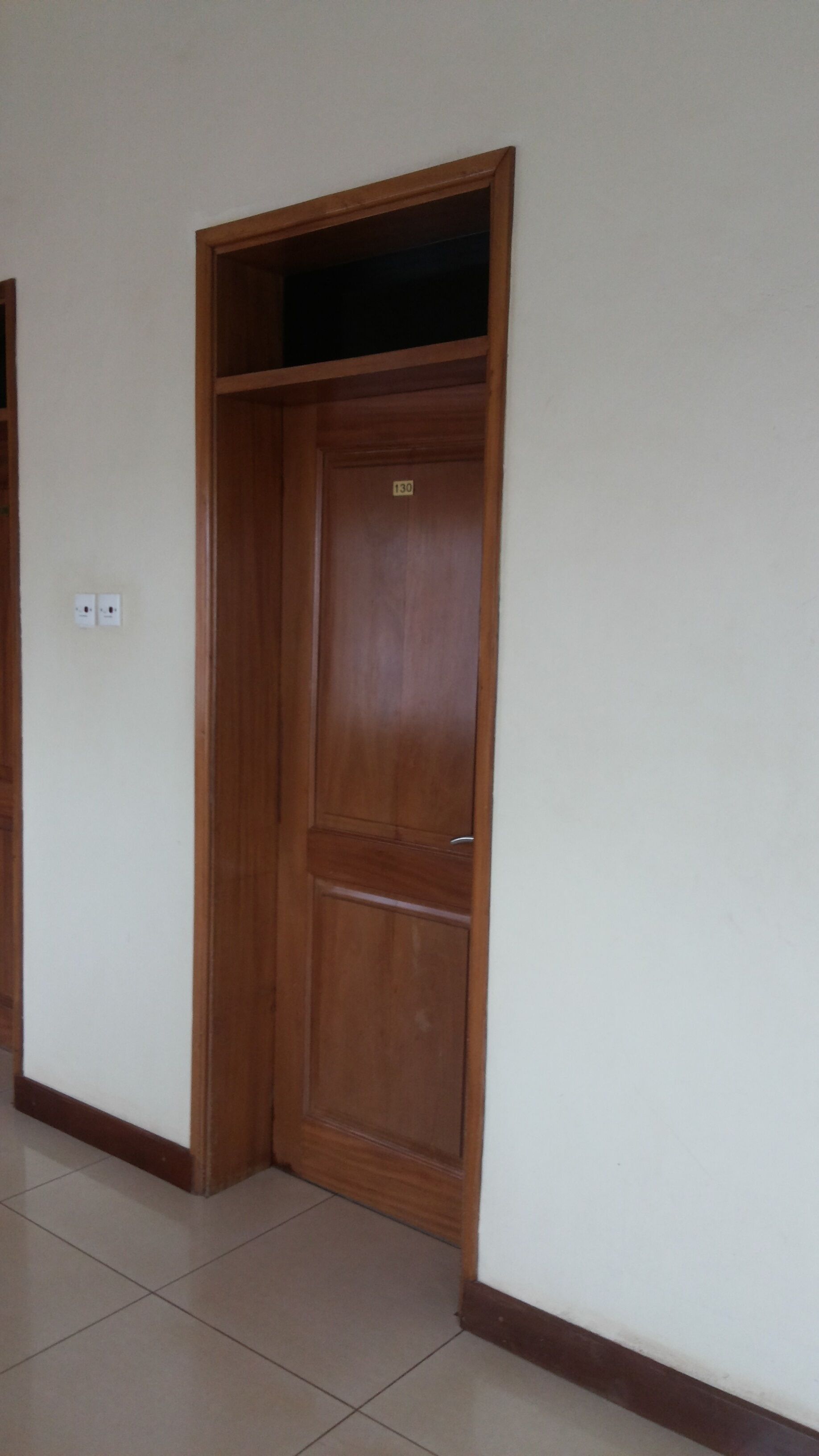 A wooden door with a number plate, a tiled floor, and a white wall.
