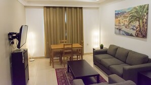 A living room with a sofa, a dining table with chairs, a TV, and a painting on the wall. - Royal Residence Hotel (Kuwait City)