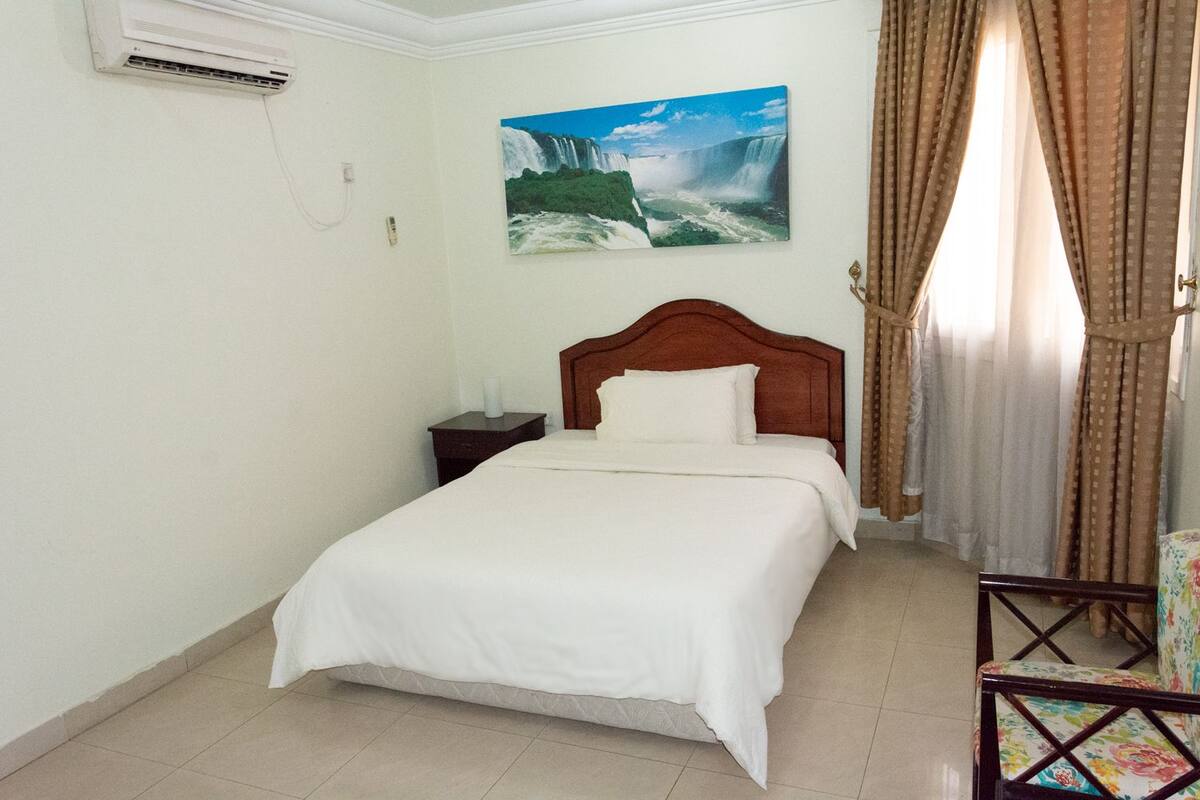 A hotel room with a bed, a nightstand, a painting of a waterfall, and a chair.