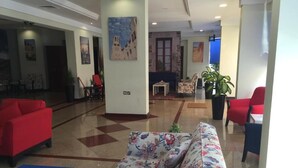 A lobby with a red sofa, a floral-patterned sofa, and a blue table. There are chairs, a small table, and a potted plant. - Royal Residence Hotel (Kuwait City)