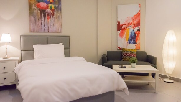 A hotel room with a bed, a nightstand, a lamp, a sofa, a coffee table, and two abstract paintings. - Royal Residence Hotel (Kuwait City)