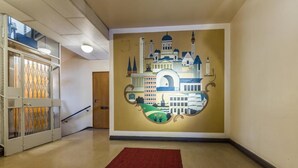 A hallway with a mural of a cityscape, a red carpet, and a staircase with a glass railing. - Go Happy Home Apt Vuorimiehenkatu 14 (Helsinki)