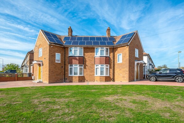 A two-story house with solar panels on the roof, a brick exterior, and a well-maintained lawn. - Goldbeaters House (Edgware)
