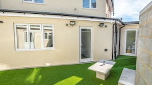A residential property with a small patio area featuring artificial grass, a white table, and a bench. - Goldbeaters House (Edgware)