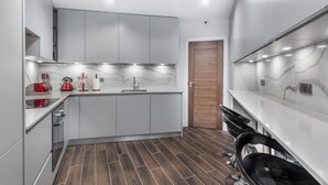A modern kitchen with grey cabinets, a marble backsplash, and a wooden door. - Goldbeaters House (Edgware)