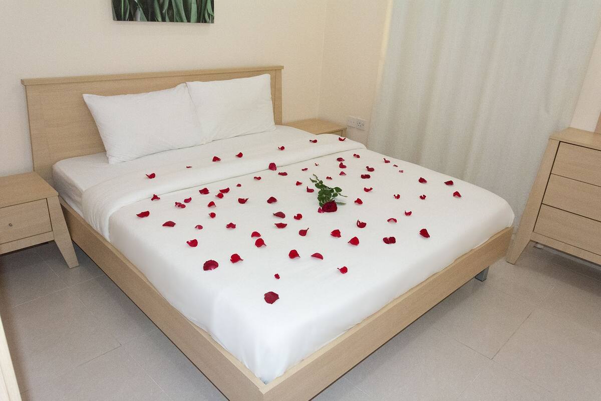 Una cama bien hecha con sábanas blancas y pétalos de rosa roja esparcidos por la superficie.