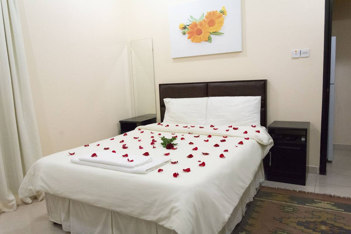 Una cama bien hecha con sábanas blancas y pétalos de rosa roja esparcidos.
