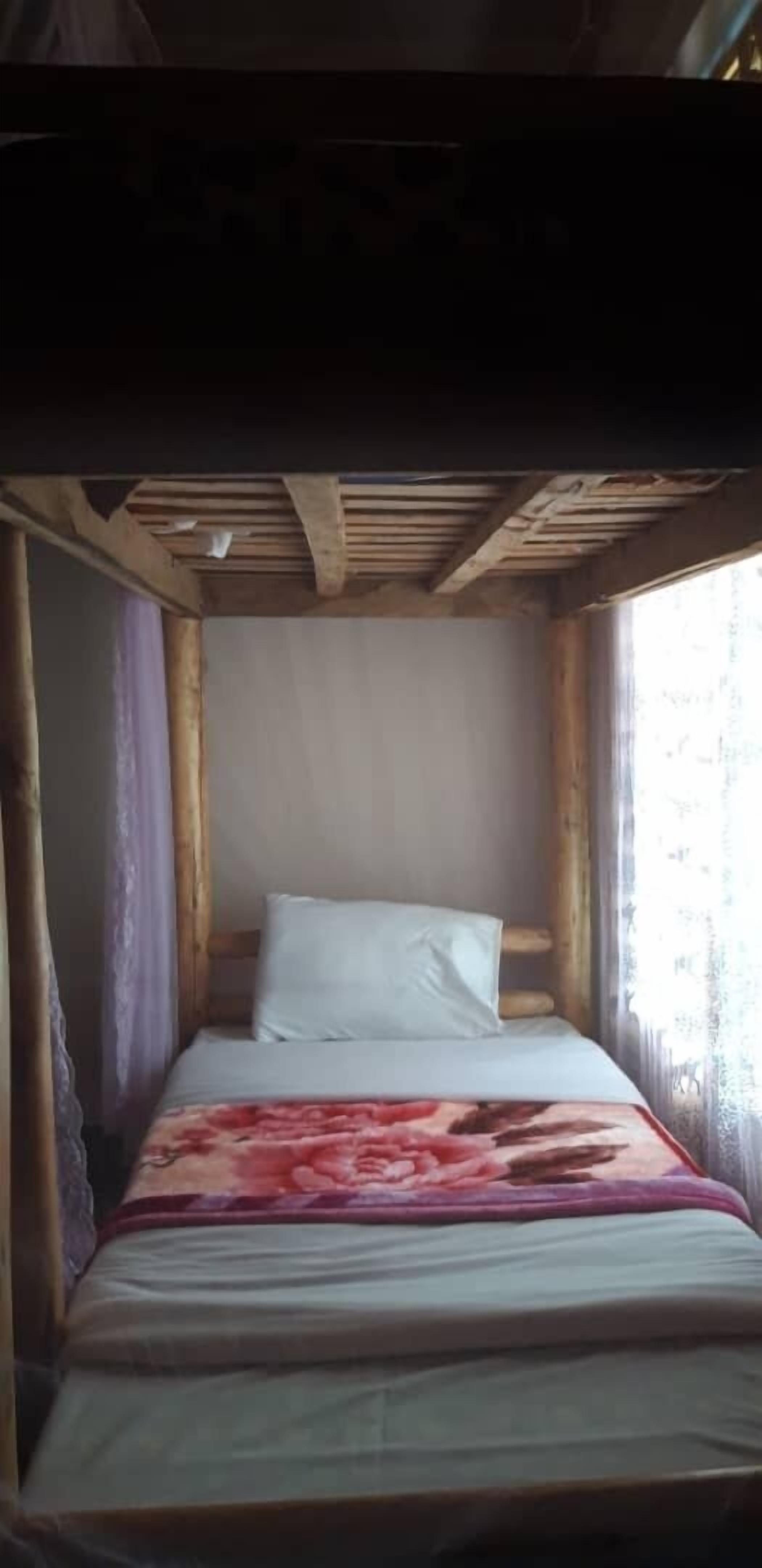 A single bed with a floral bedspread in a room with wooden beams and a window with curtains.