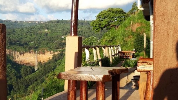 A wooden bench overlooking a lush valley with a stone wall and a wooden railing. - Rafiki Lodge Sipi (Sipi)