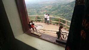 A view from a window overlooking a scenic landscape with a wooden railing and a bicycle in the foreground. - Rafiki Lodge Sipi (Sipi)
