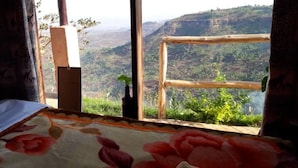 A room with a bed, a window with a view of a mountainous landscape, and a wooden frame. - Rafiki Lodge Sipi (Sipi)