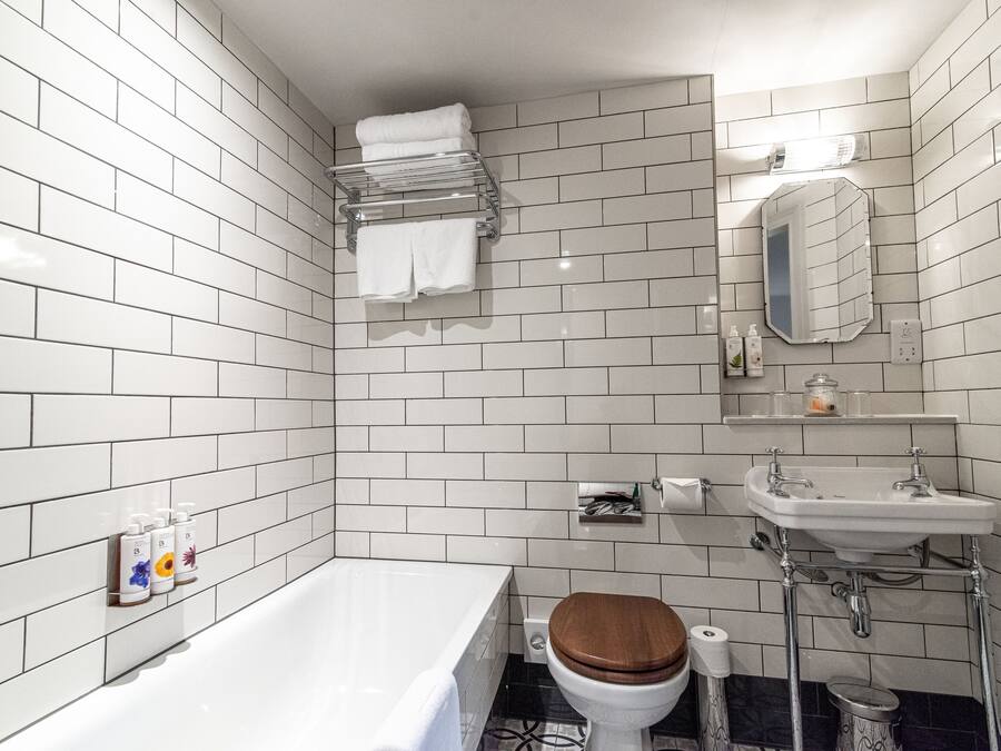 A modern bathroom with white tiled walls, a white bathtub, a wooden toilet seat, a white sink, and a mirror above the sink.