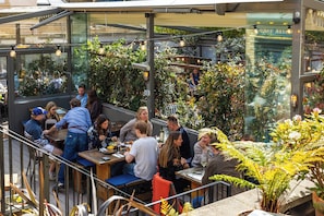 An outdoor dining area with tables and chairs, surrounded by greenery and a glass enclosure. - Aragon House (London)