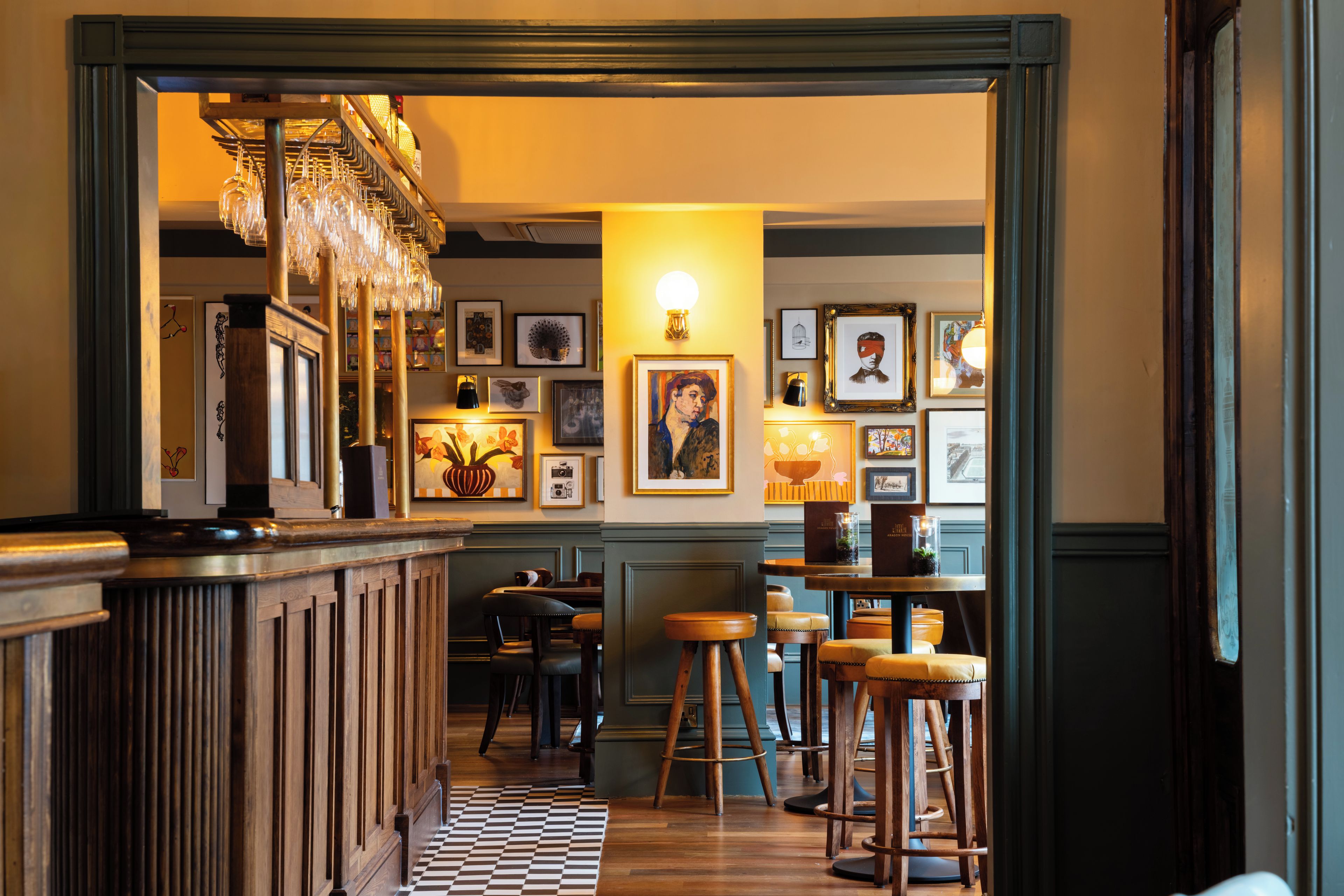 Un'area bar con sgabelli di legno, pavimento a scacchi e opere d'arte incorniciate alle pareti.