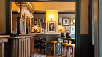 A bar area with wooden stools, a checkered floor, and framed artwork on the walls.
