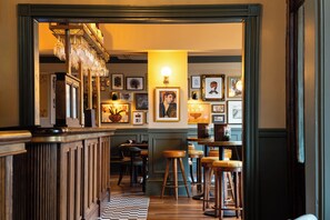 A bar area with wooden stools, a checkered floor, and framed artwork on the walls. - Aragon House (London)