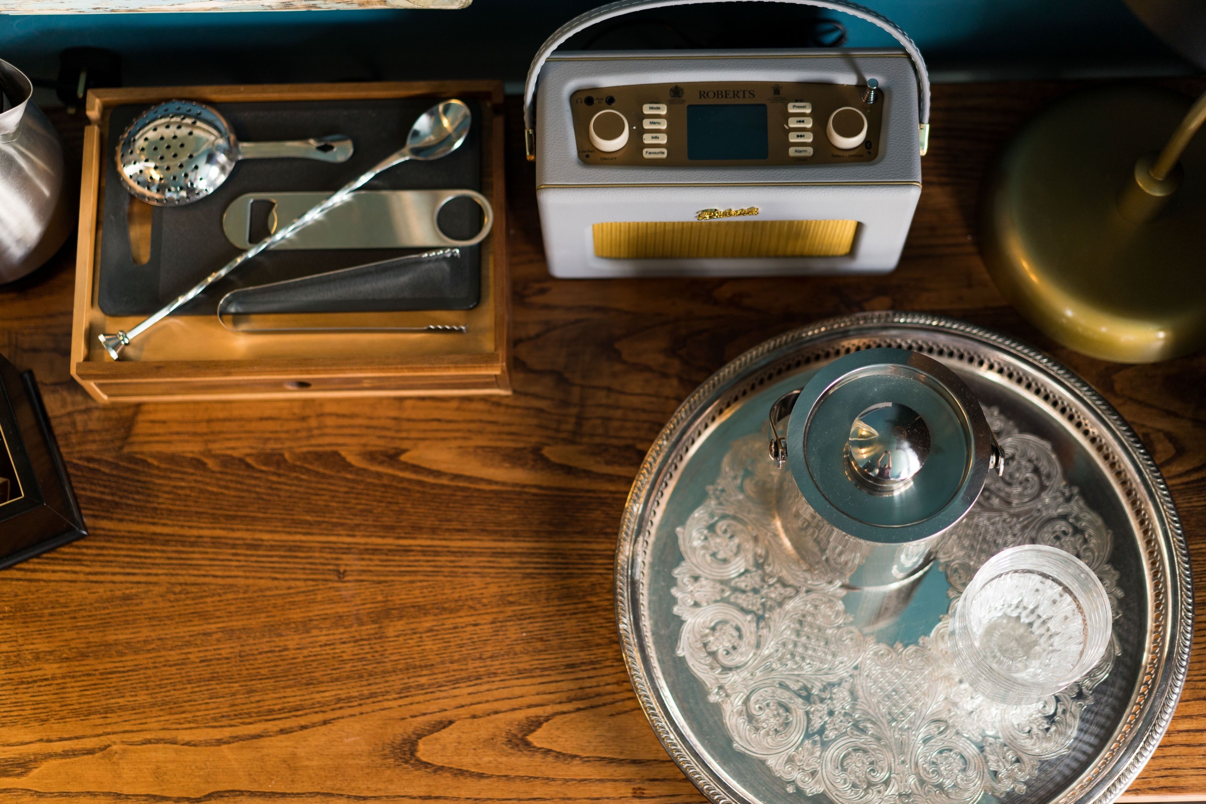 Una mesa de madera con una radio, una bandeja con tapa de vidrio decorativa y un recipiente metálico.
