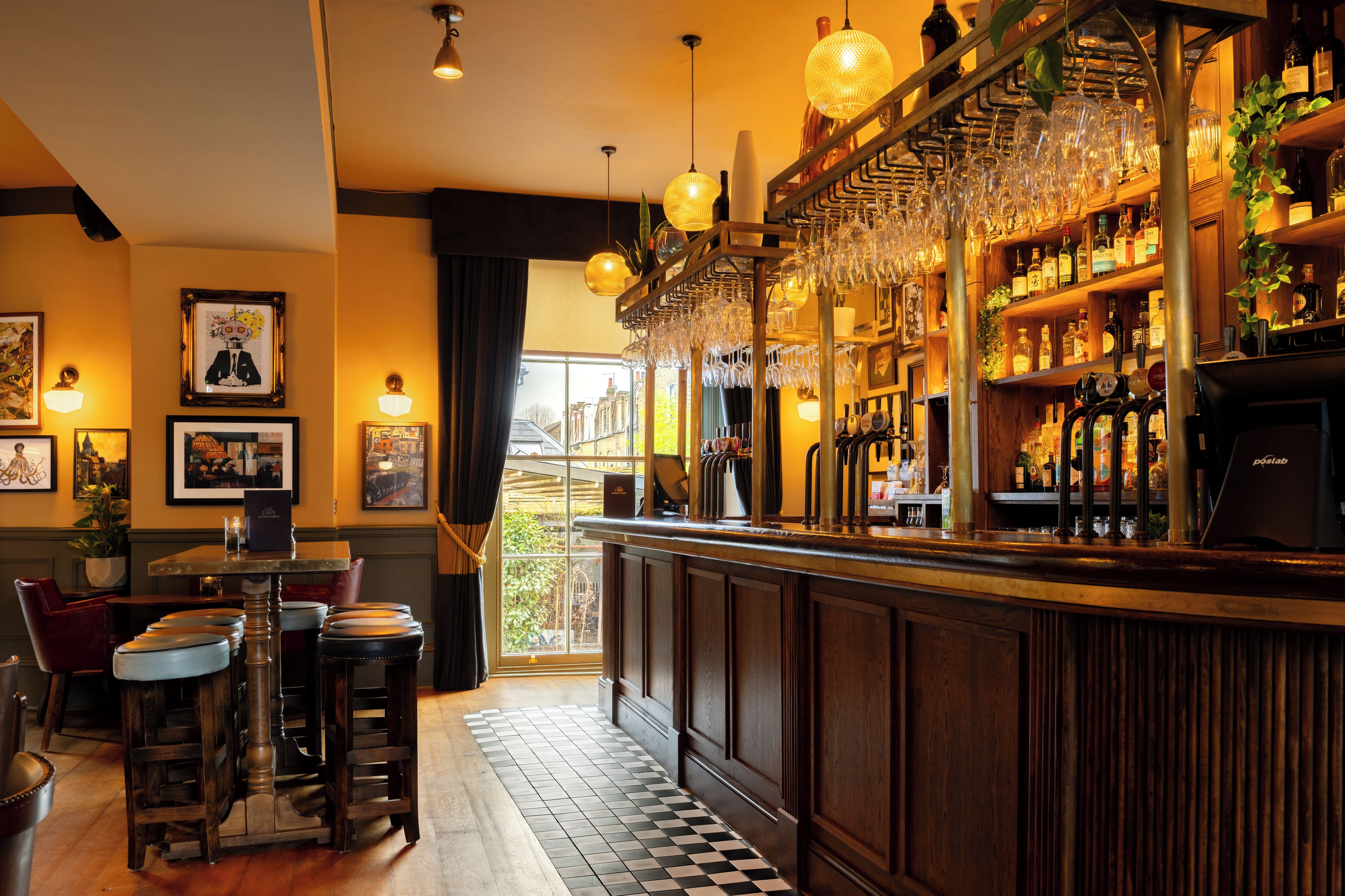 Zona de bar con taburetes, barra y una variedad de botellas y vasos.
