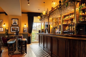 A bar area with stools, a bar counter, and a variety of bottles and glasses. - Aragon House (London)