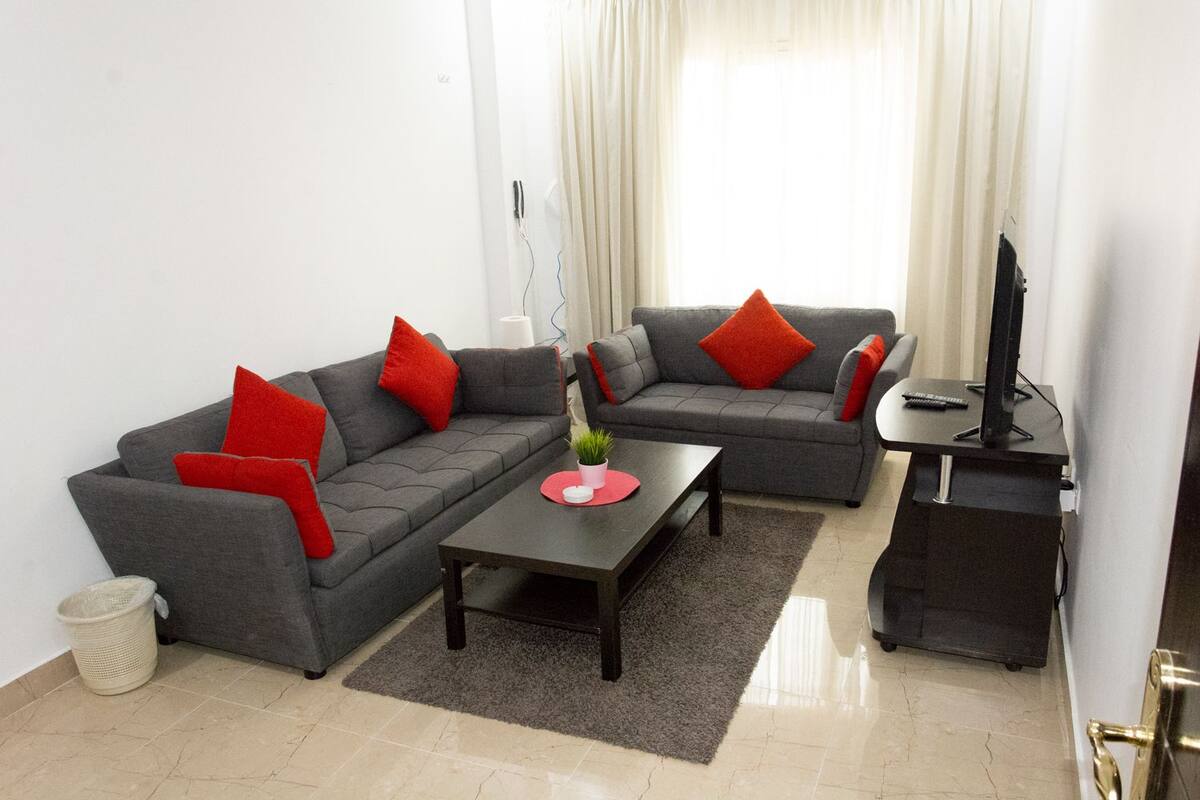 A modern living room with a grey sofa, red cushions, a coffee table, and a TV stand.
