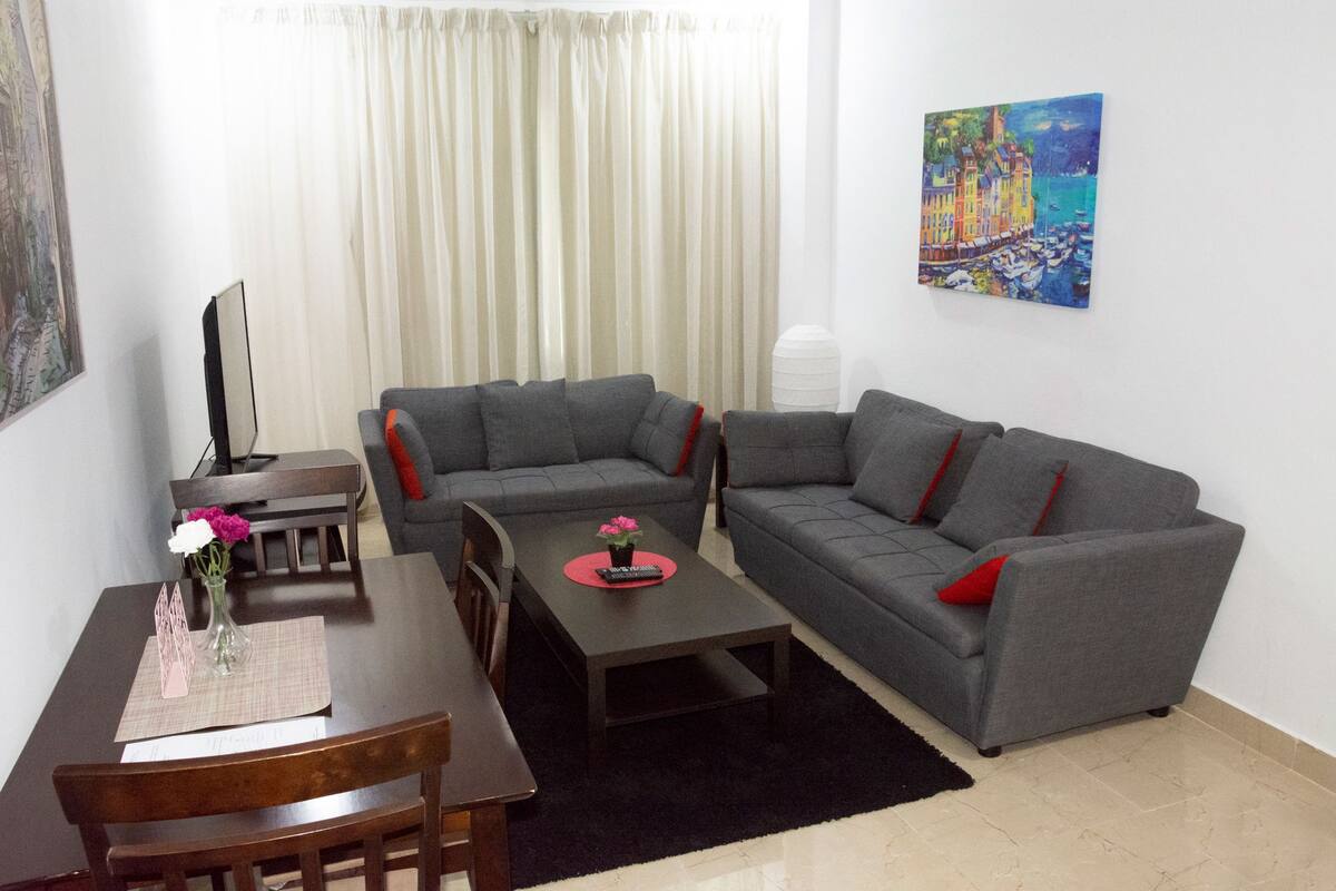 A living room with a grey sofa, a wooden coffee table, and a dining table with chairs.