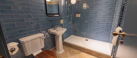 A bathroom with blue tiled walls, a wooden floor, a white sink, a toilet, and a shower.