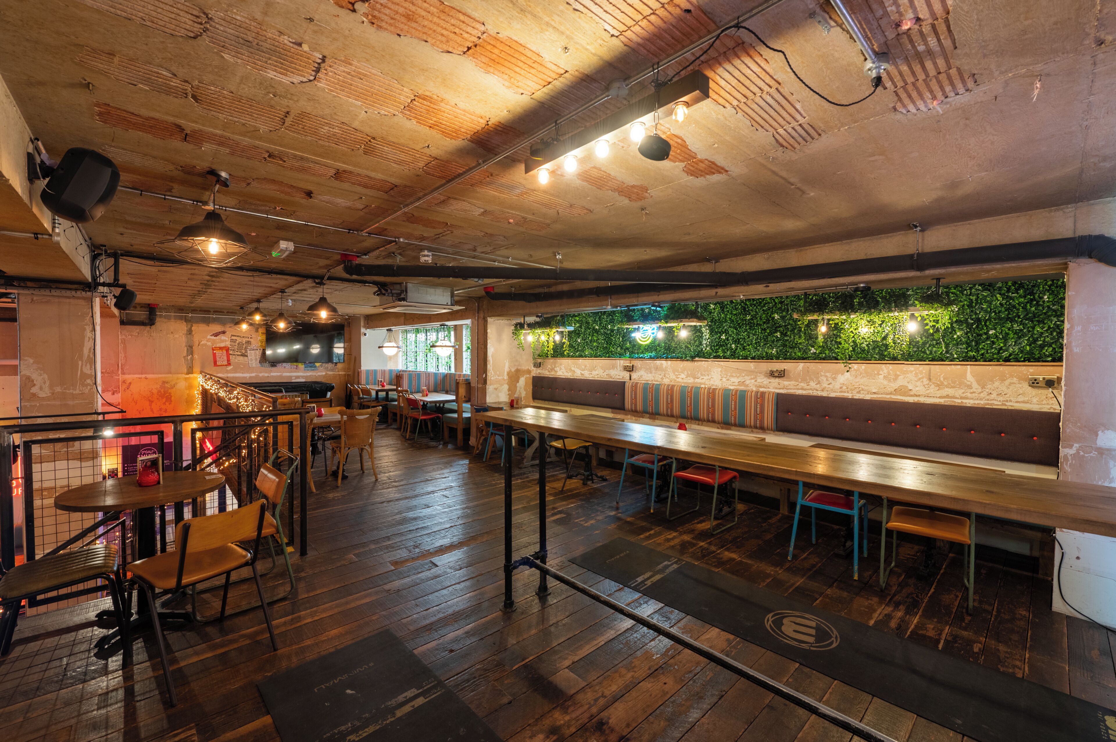 Un restaurante con suelos de madera, una barra larga y una pared verde con plantas.