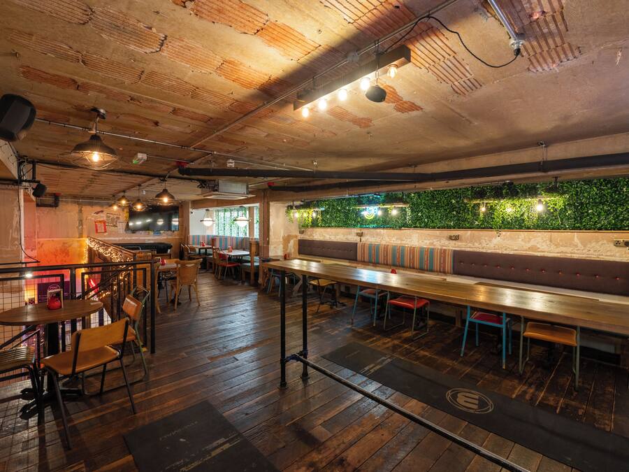 Un restaurante con suelos de madera, una barra larga y una pared verde con plantas.