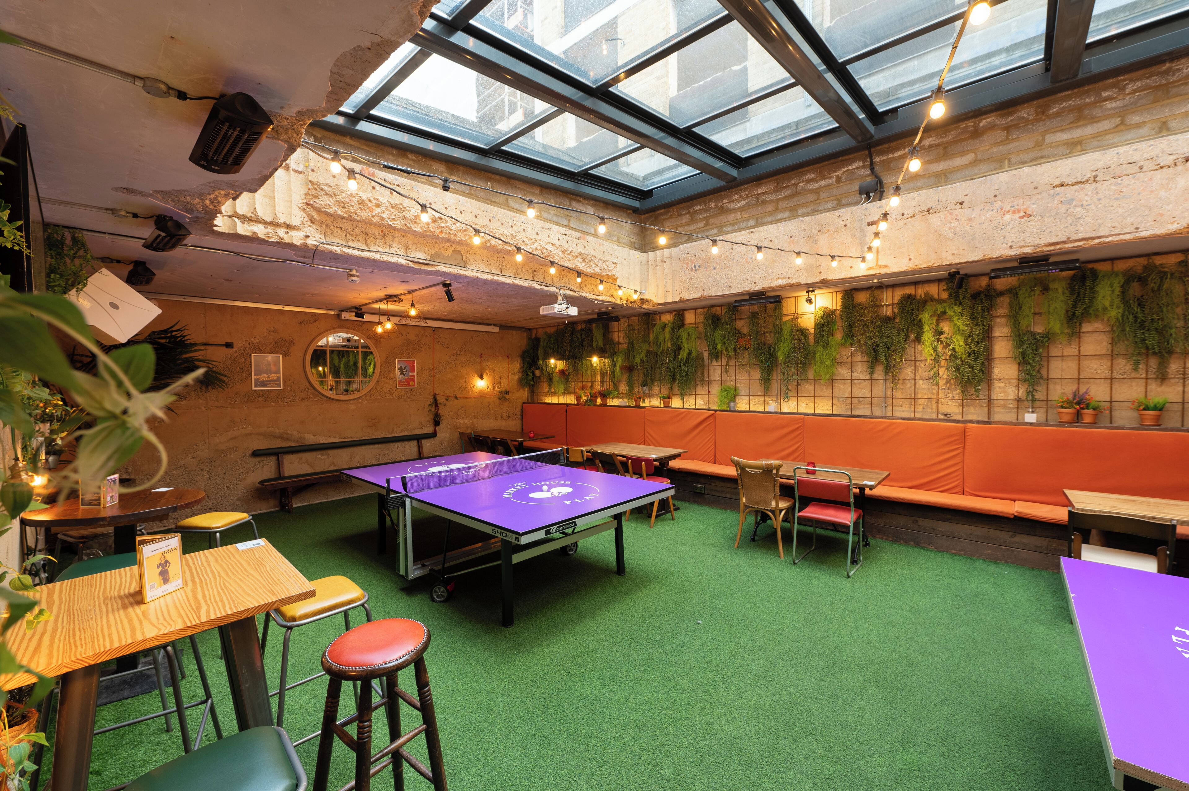 Una habitación con mesa de ping pong, césped artificial verde y asientos anaranjados.