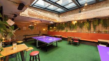 Una habitación con mesa de ping pong, césped artificial verde y asientos anaranjados.